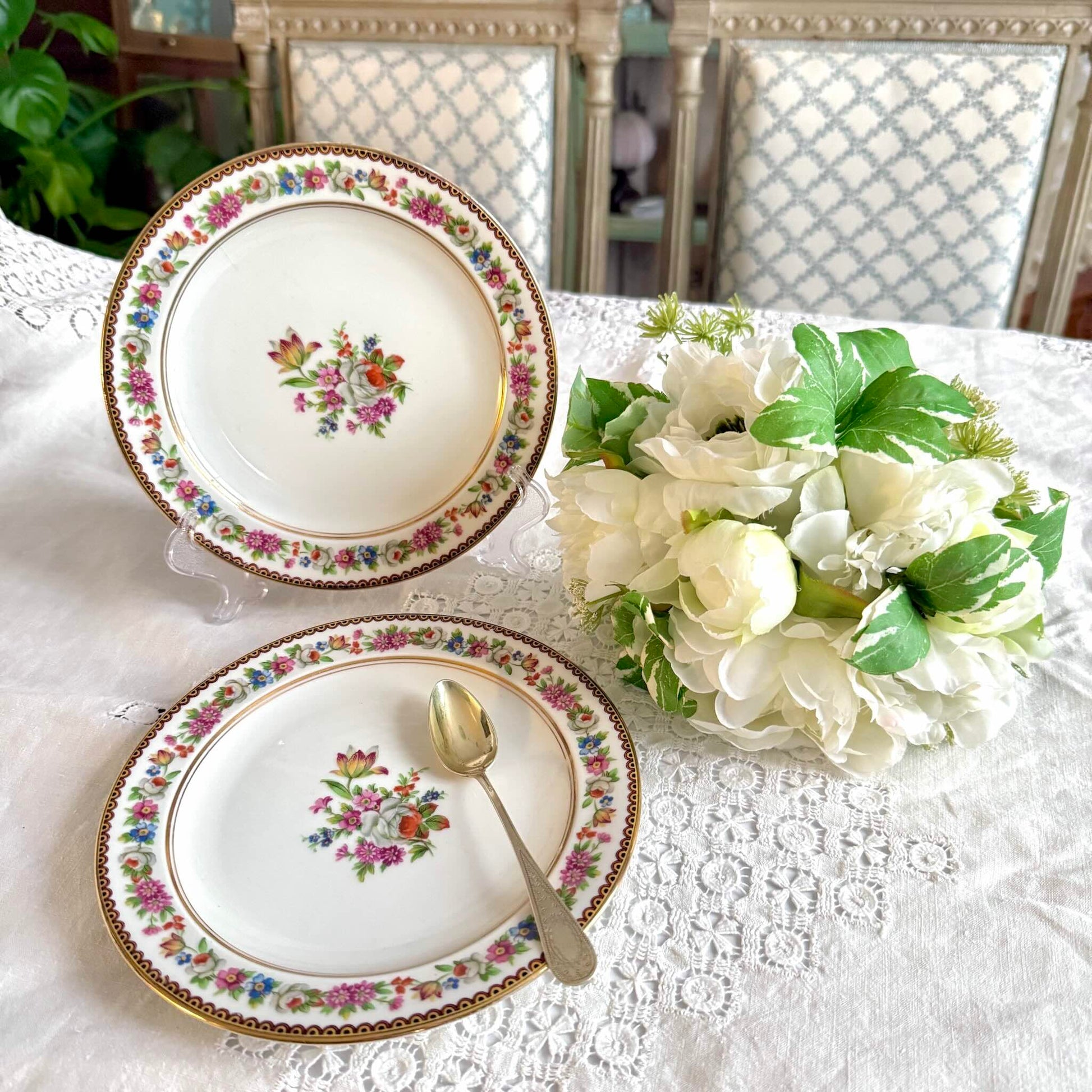 Raynaud Limoges floral porcelain dessert plates, set of two, early 20th century, featuring a central flower bouquet, floral garland border, and triple gilded rims.