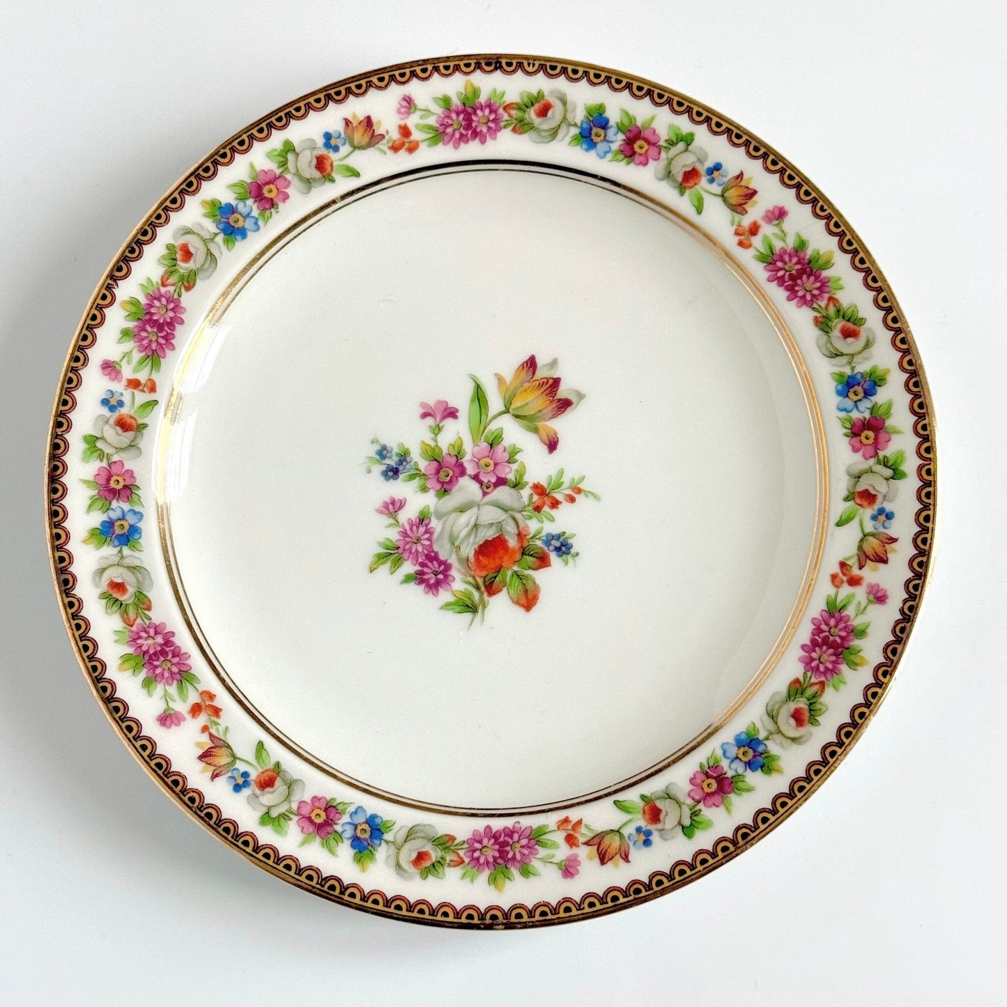 Raynaud Limoges floral porcelain dessert plates, set of two, early 20th century, featuring a central flower bouquet, floral garland border, and triple gilded rims.