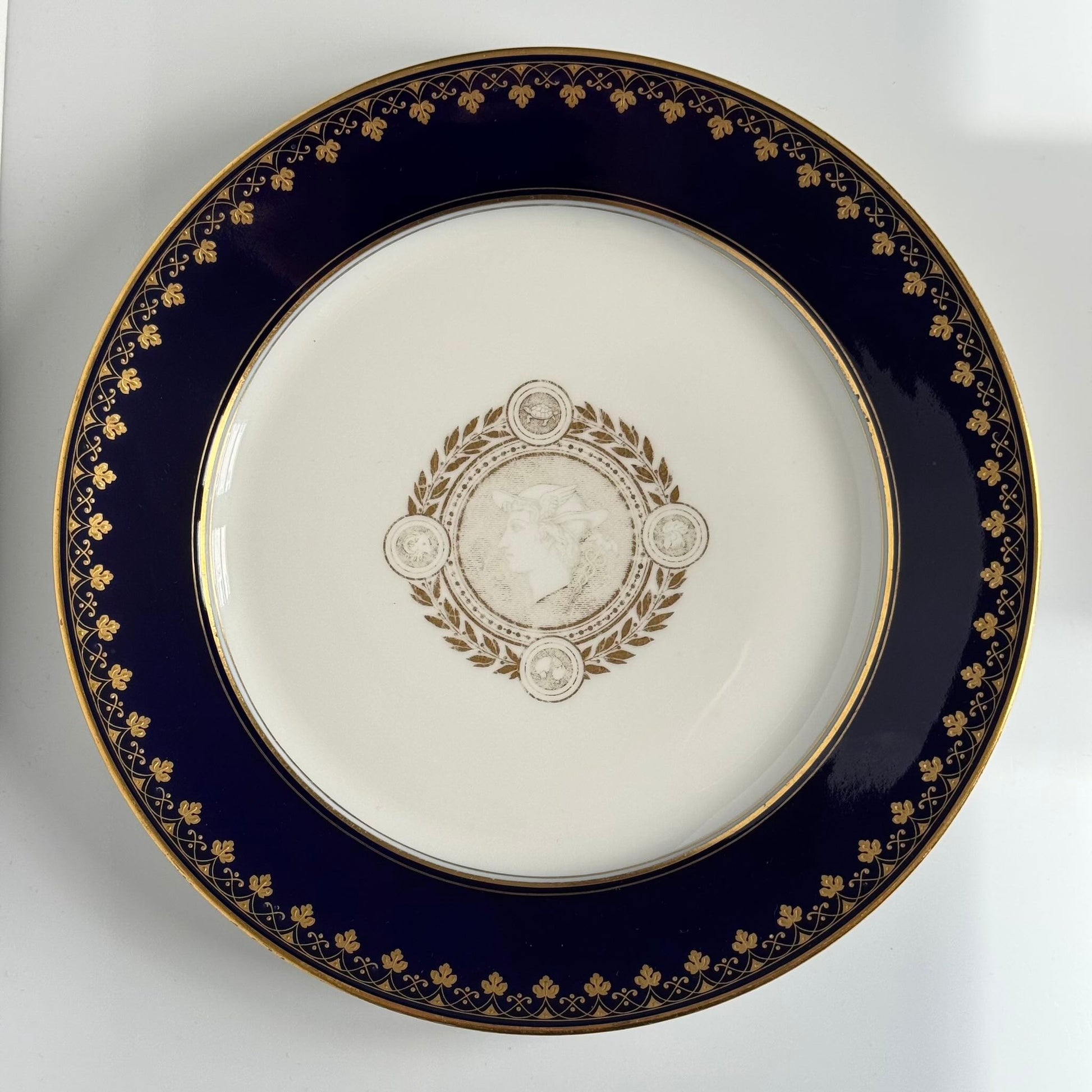 English: Sèvres porcelain plate, neoclassical style, with cobalt-blue border and gilded motifs of Mercury, laurel leaves, and symbolic animals, 1882–1883; 日本語: セーヴル製磁器プレート、新古典主義様式、コバルトブルーの縁に金彩装飾、メルクリウスと象徴的な動物、1882–1883年; Français: Assiette en porcelaine de Sèvres, style néoclassique, bordure bleu de Sèvres et motifs dorés de Mercure, laurier et animaux symboliques, 1882–1883.