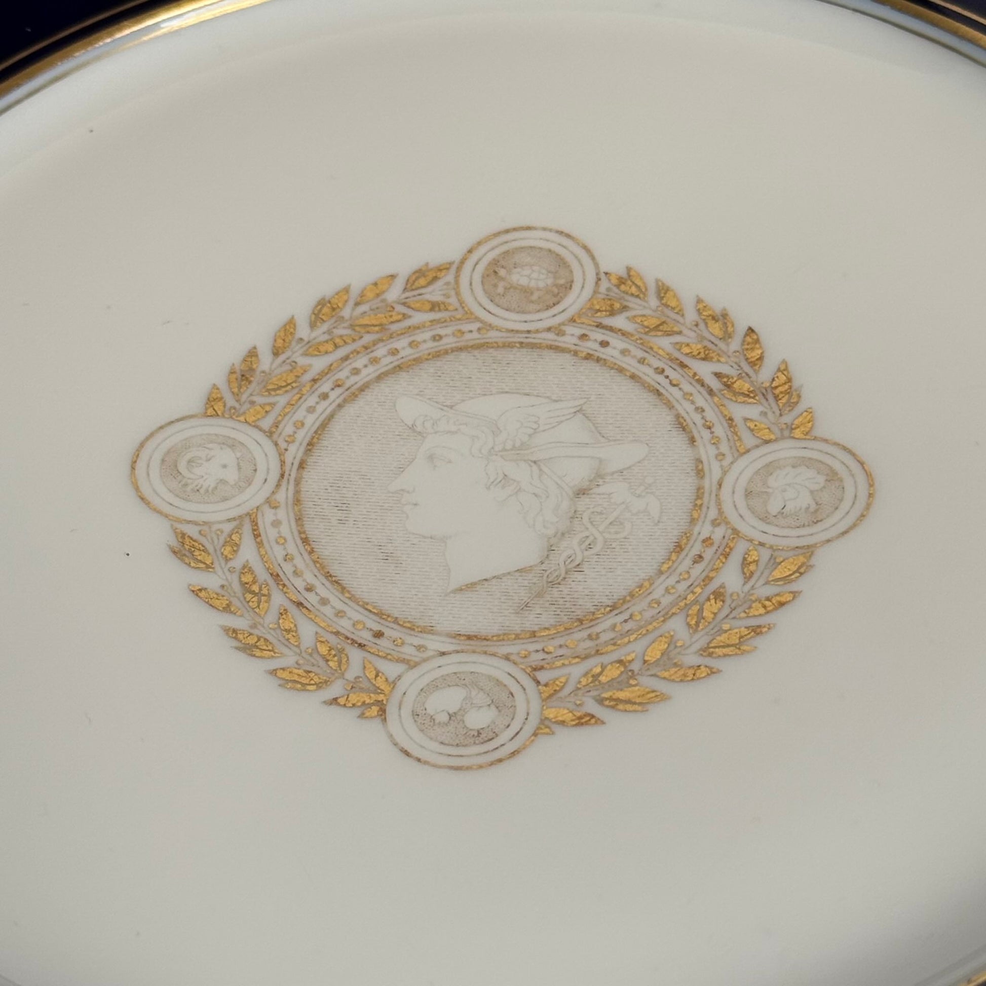 English: Sèvres porcelain plate, neoclassical style, with cobalt-blue border and gilded motifs of Mercury, laurel leaves, and symbolic animals, 1882–1883; 日本語: セーヴル製磁器プレート、新古典主義様式、コバルトブルーの縁に金彩装飾、メルクリウスと象徴的な動物、1882–1883年; Français: Assiette en porcelaine de Sèvres, style néoclassique, bordure bleu de Sèvres et motifs dorés de Mercure, laurier et animaux symboliques, 1882–1883.