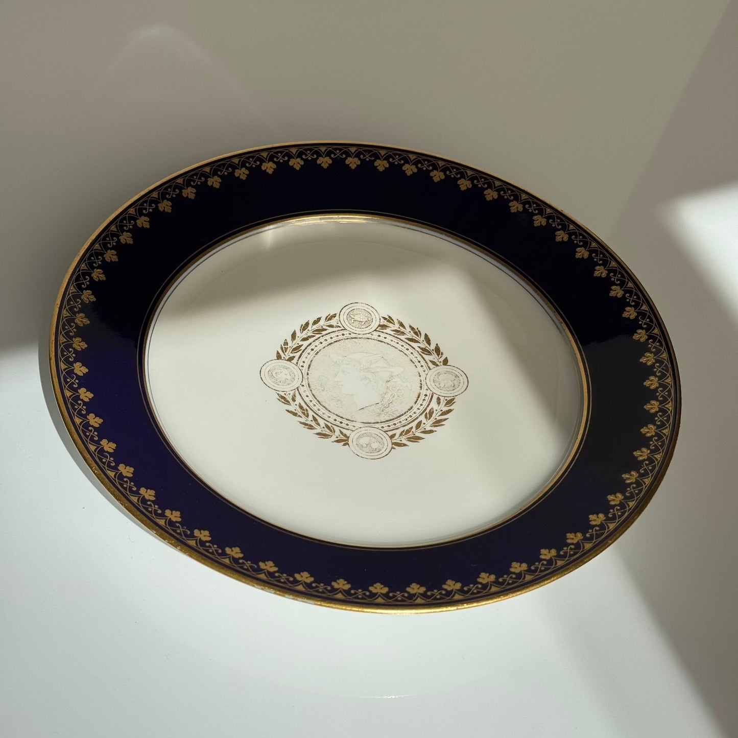 English: Sèvres porcelain plate, neoclassical style, with cobalt-blue border and gilded motifs of Mercury, laurel leaves, and symbolic animals, 1882–1883; 日本語: セーヴル製磁器プレート、新古典主義様式、コバルトブルーの縁に金彩装飾、メルクリウスと象徴的な動物、1882–1883年; Français: Assiette en porcelaine de Sèvres, style néoclassique, bordure bleu de Sèvres et motifs dorés de Mercure, laurier et animaux symboliques, 1882–1883.
