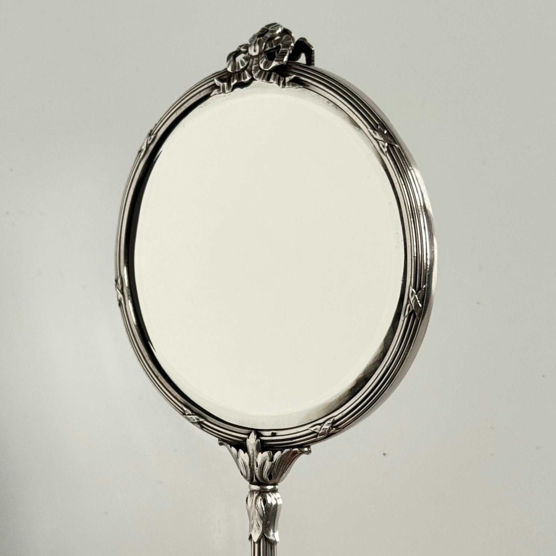 English: Silver plate hand mirror in Louis XVI style with crossed ribbons and decorative bow, late 19th to early 20th century, double-sided mirror ; 日本語: ルイ16世様式の銀メッキ手鏡、リボンと装飾的な結び目付き、19世紀末～20世紀初頭、両面鏡 ; Français: Miroir à main en métal argenté style Louis XVI avec rubans croisés et nœud, fin XIXe – début XXe siècle, miroir double face.