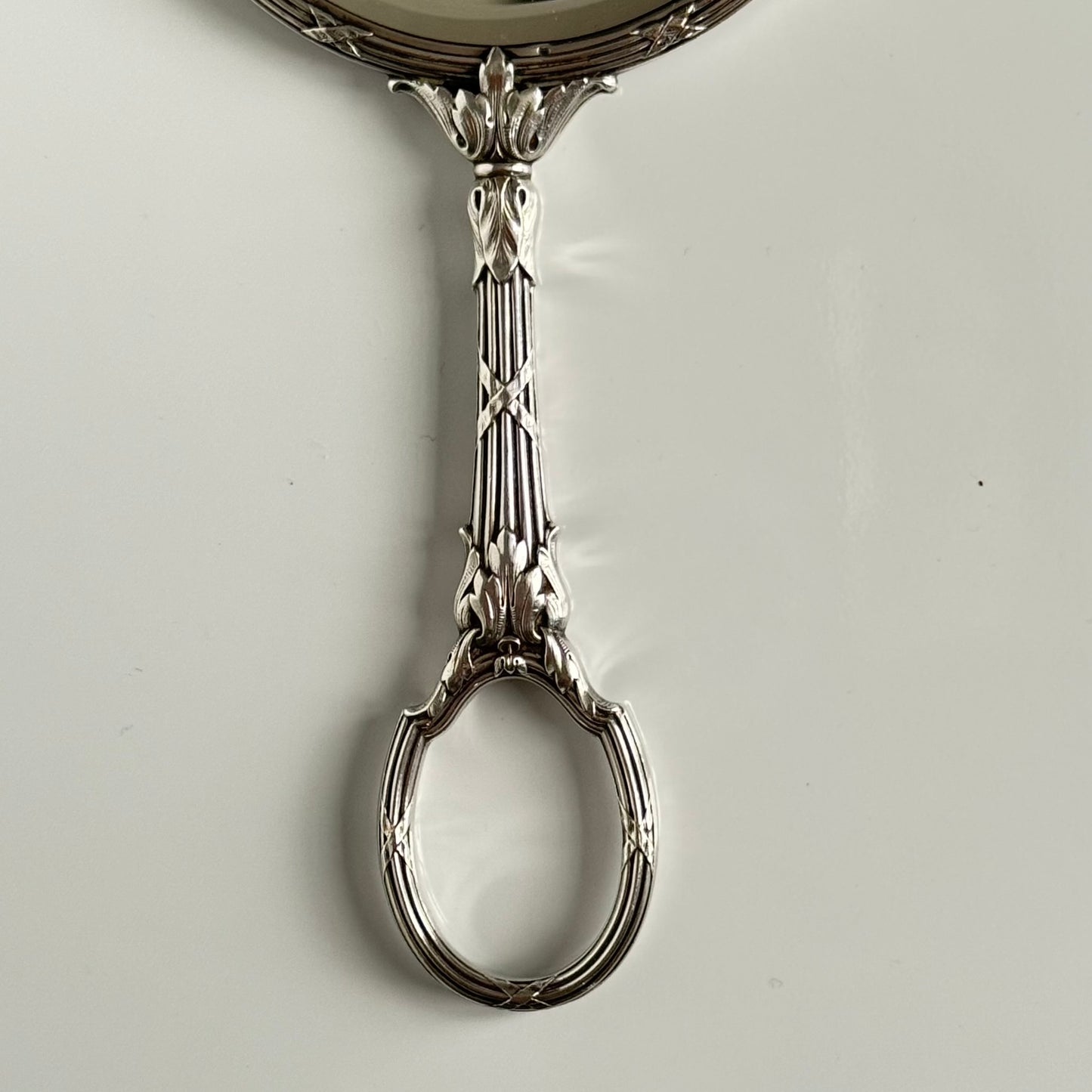 English: Silver plate hand mirror in Louis XVI style with crossed ribbons and decorative bow, late 19th to early 20th century, double-sided mirror ; 日本語: ルイ16世様式の銀メッキ手鏡、リボンと装飾的な結び目付き、19世紀末～20世紀初頭、両面鏡 ; Français: Miroir à main en métal argenté style Louis XVI avec rubans croisés et nœud, fin XIXe – début XXe siècle, miroir double face.