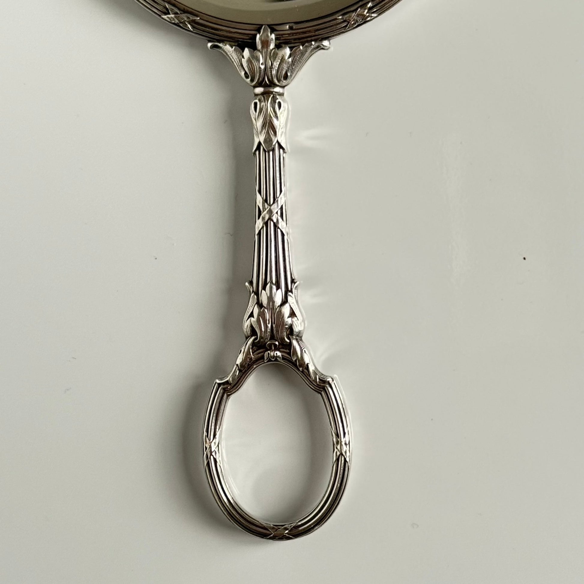 English: Silver plate hand mirror in Louis XVI style with crossed ribbons and decorative bow, late 19th to early 20th century, double-sided mirror ; 日本語: ルイ16世様式の銀メッキ手鏡、リボンと装飾的な結び目付き、19世紀末～20世紀初頭、両面鏡 ; Français: Miroir à main en métal argenté style Louis XVI avec rubans croisés et nœud, fin XIXe – début XXe siècle, miroir double face.
