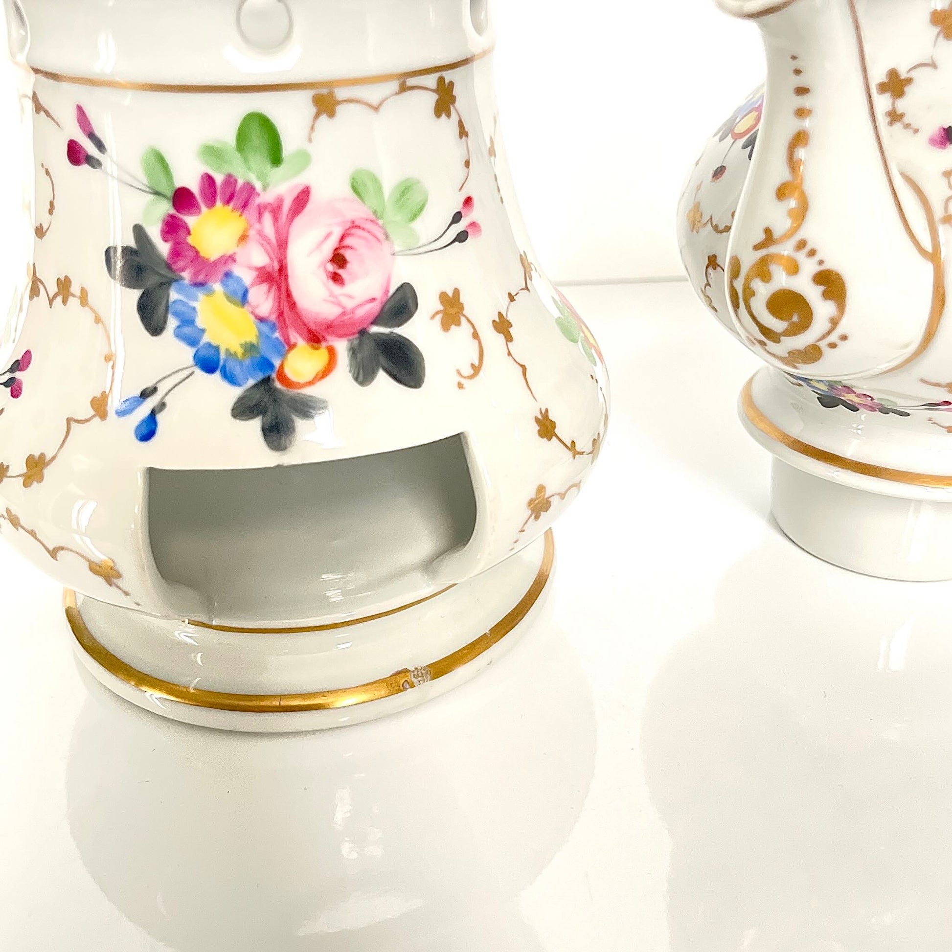 This is a Paris porcelain tisanière (herbal teapot with warmer) from the early 20th century. It features a hand-painted polychrome floral design with gilded accents.