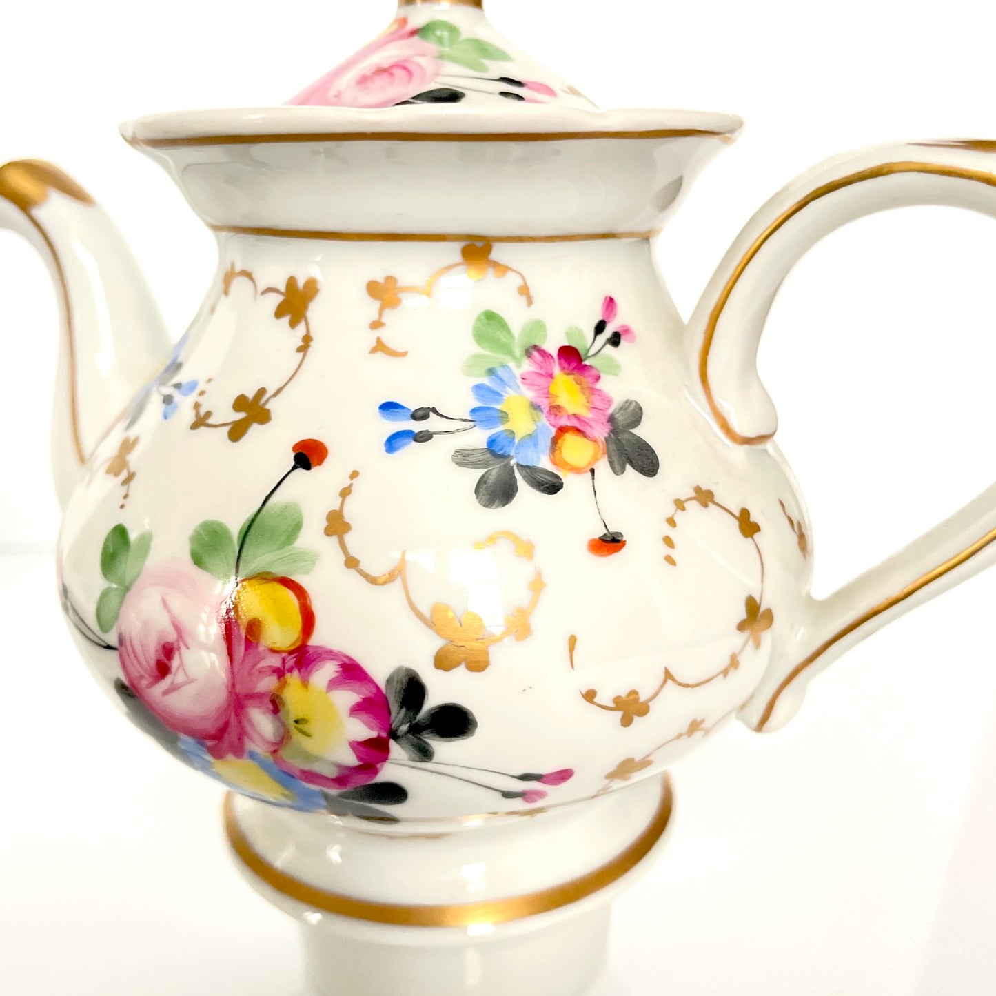 This is a Paris porcelain tisanière (herbal teapot with warmer) from the early 20th century. It features a hand-painted polychrome floral design with gilded accents.