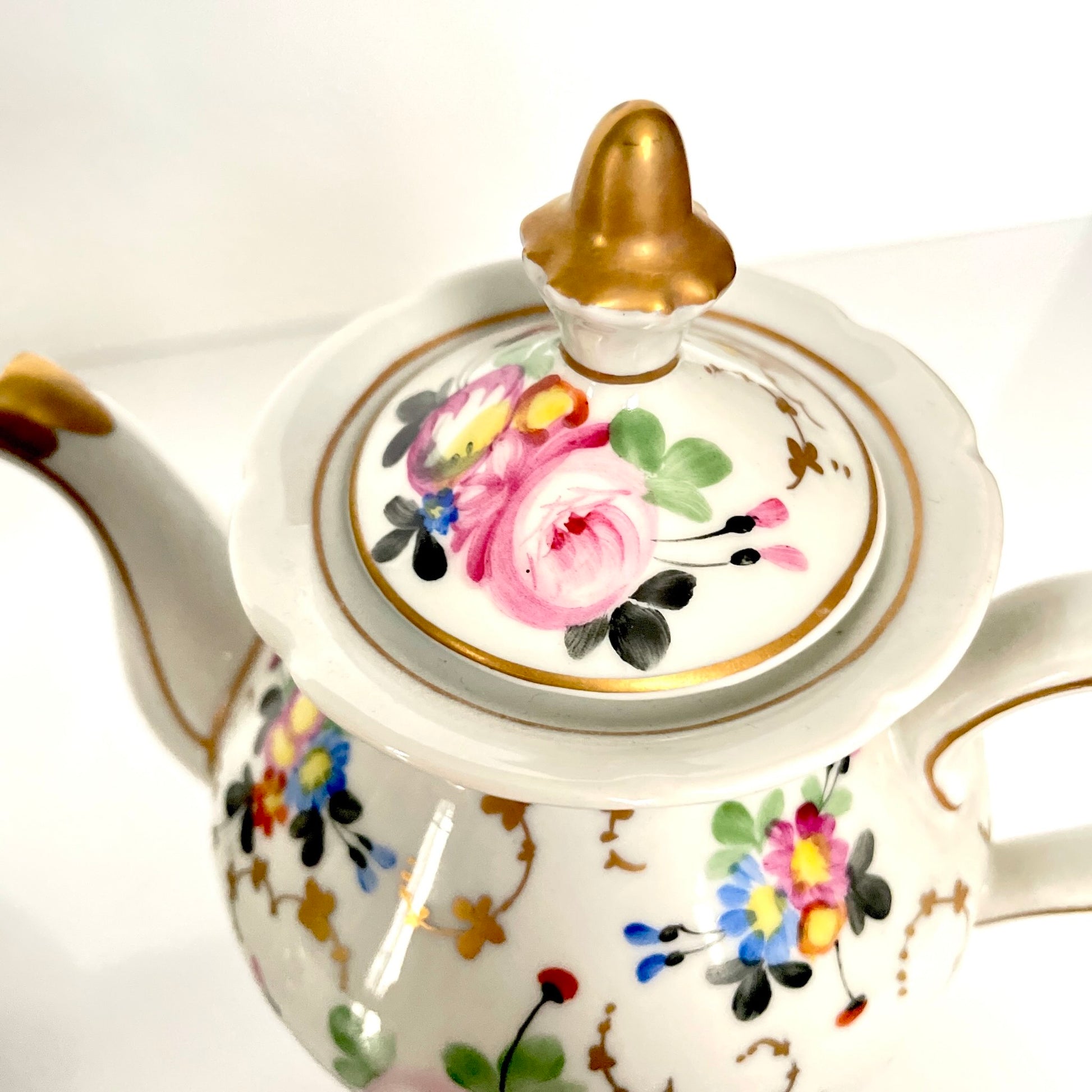 This is a Paris porcelain tisanière (herbal teapot with warmer) from the early 20th century. It features a hand-painted polychrome floral design with gilded accents.