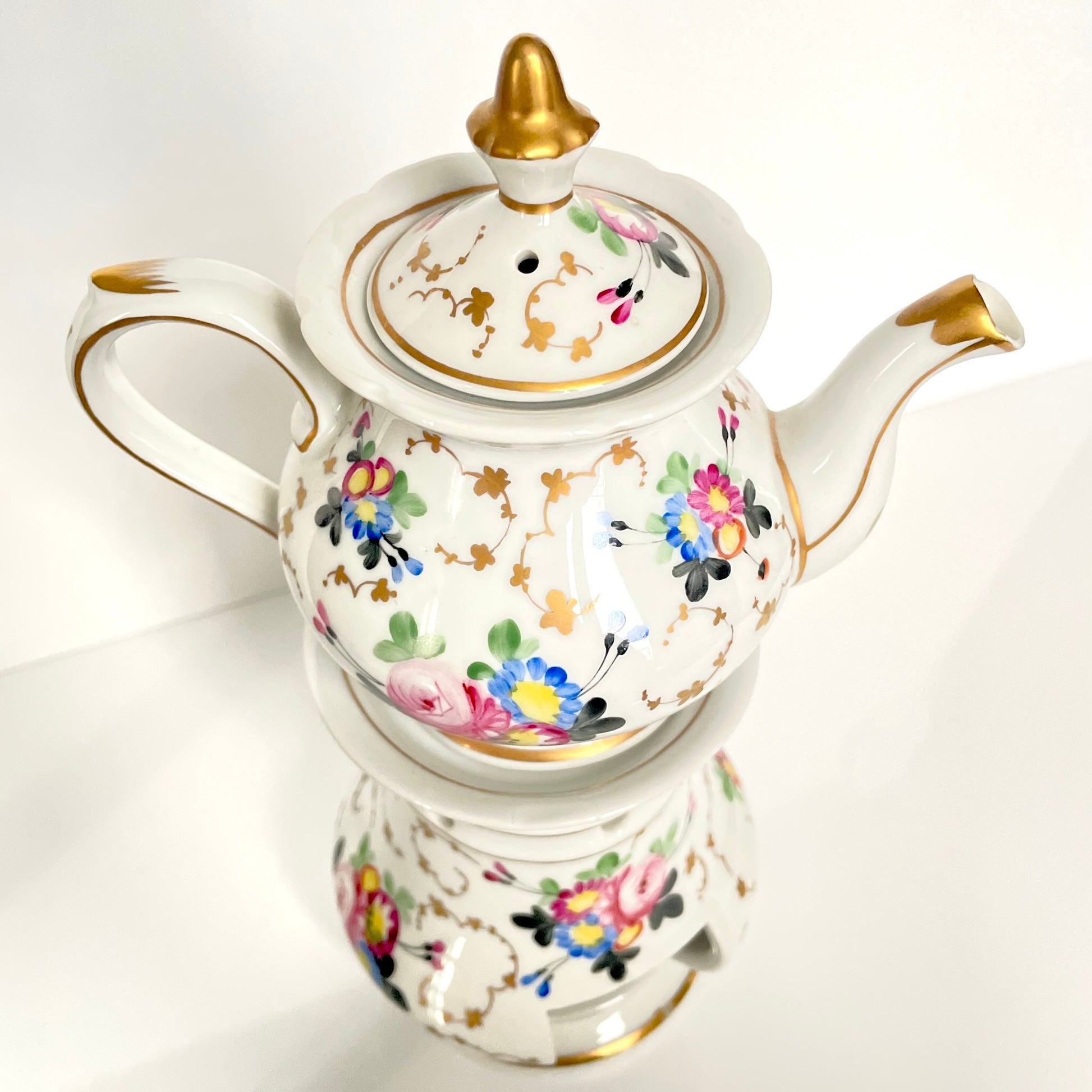 This is a Paris porcelain tisanière (herbal teapot with warmer) from the early 20th century. It features a hand-painted polychrome floral design with gilded accents.