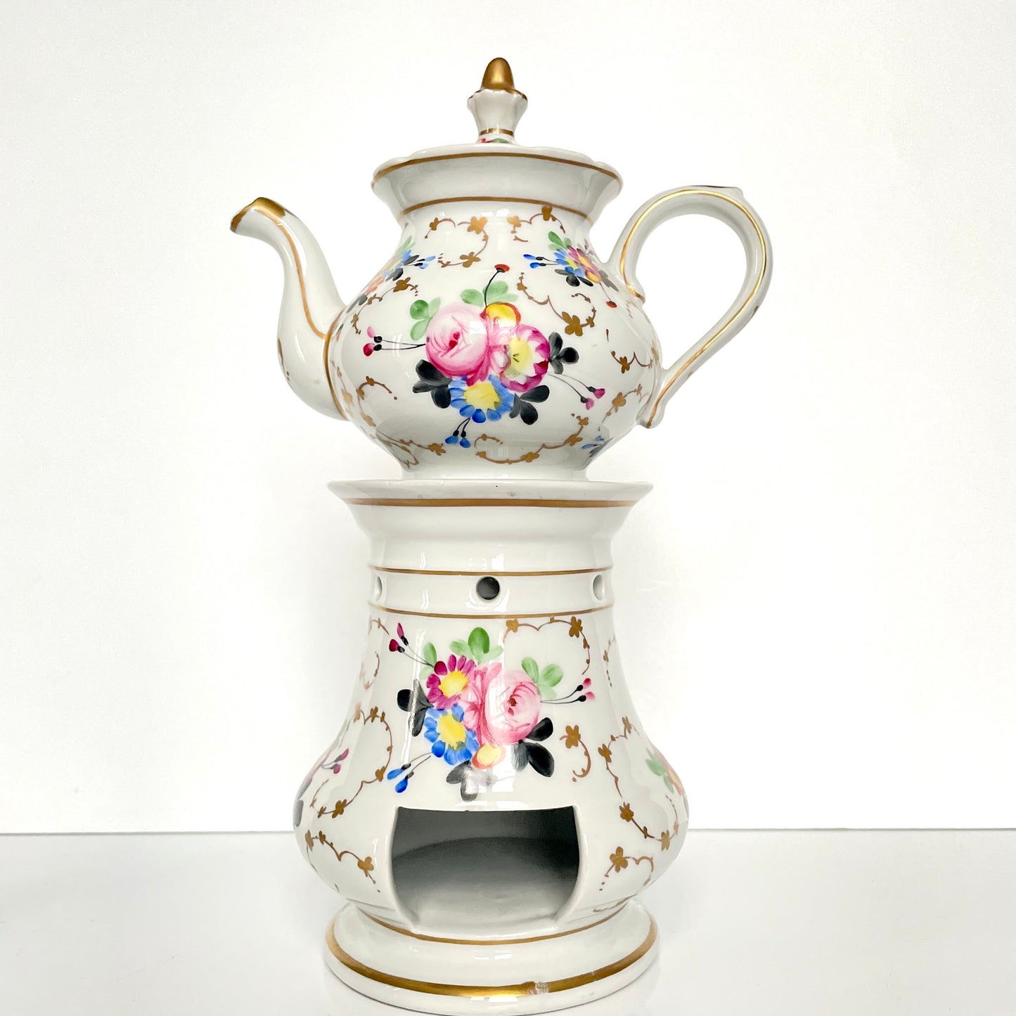 This is a Paris porcelain tisanière (herbal teapot with warmer) from the early 20th century. It features a hand-painted polychrome floral design with gilded accents.