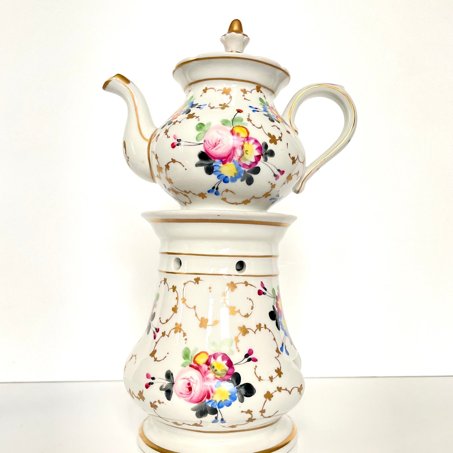 This is a Paris porcelain tisanière (herbal teapot with warmer) from the early 20th century. It features a hand-painted polychrome floral design with gilded accents.