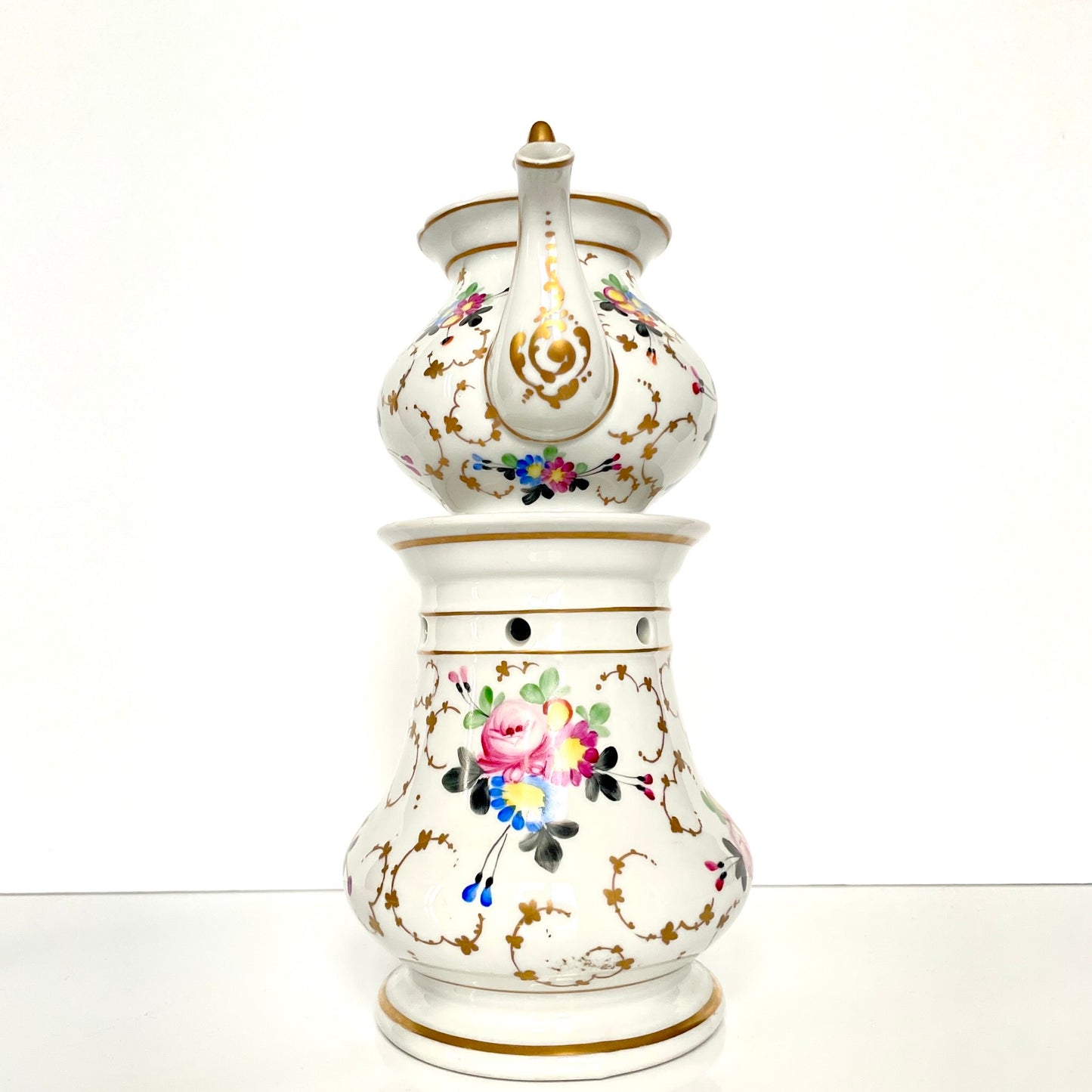 This is a Paris porcelain tisanière (herbal teapot with warmer) from the early 20th century. It features a hand-painted polychrome floral design with gilded accents.