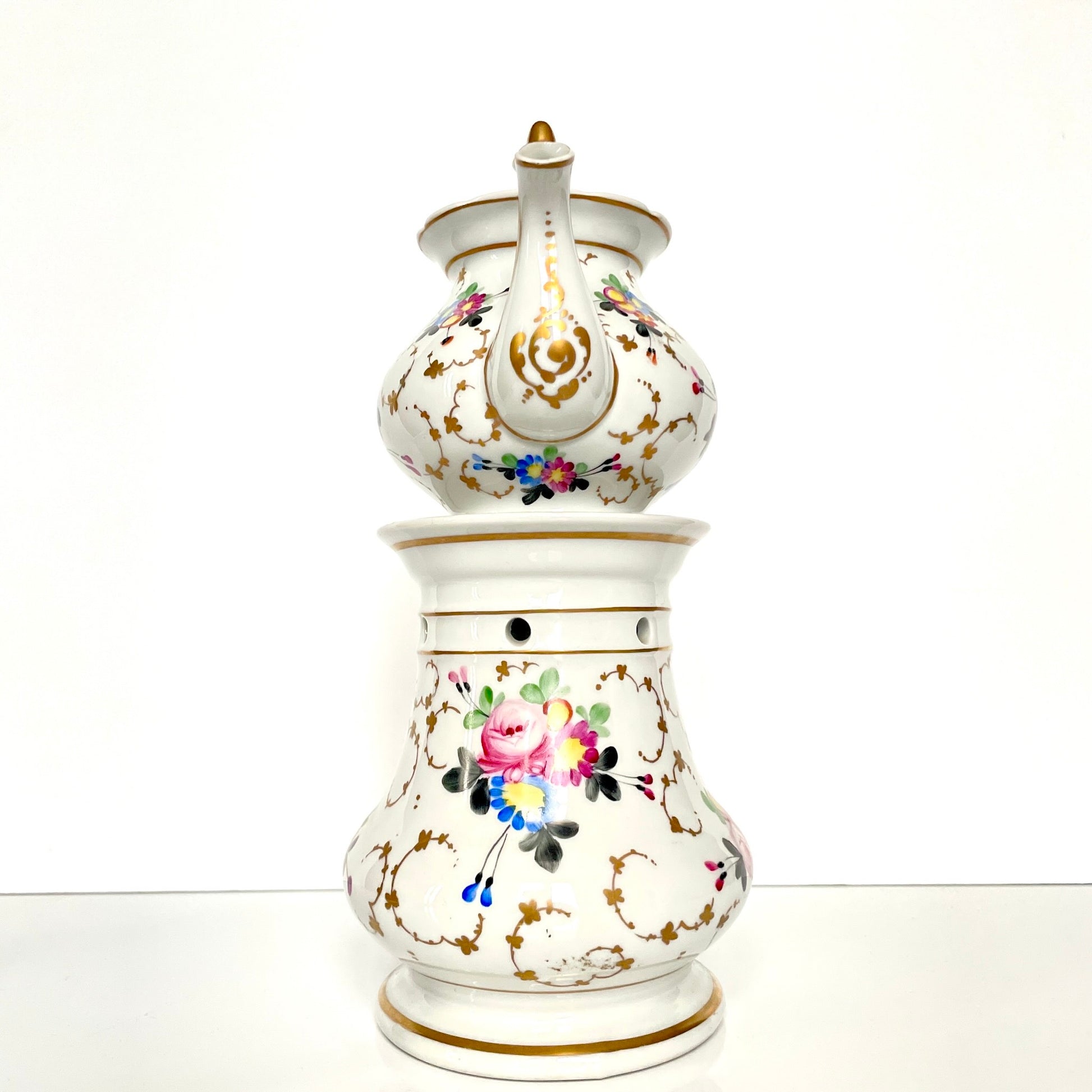 This is a Paris porcelain tisanière (herbal teapot with warmer) from the early 20th century. It features a hand-painted polychrome floral design with gilded accents.