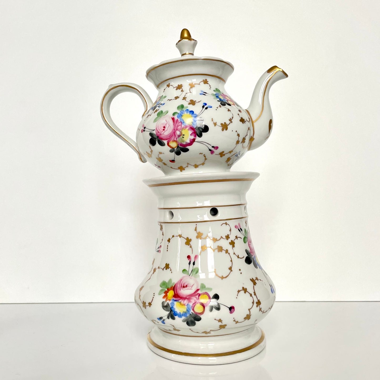 This is a Paris porcelain tisanière (herbal teapot with warmer) from the early 20th century. It features a hand-painted polychrome floral design with gilded accents.