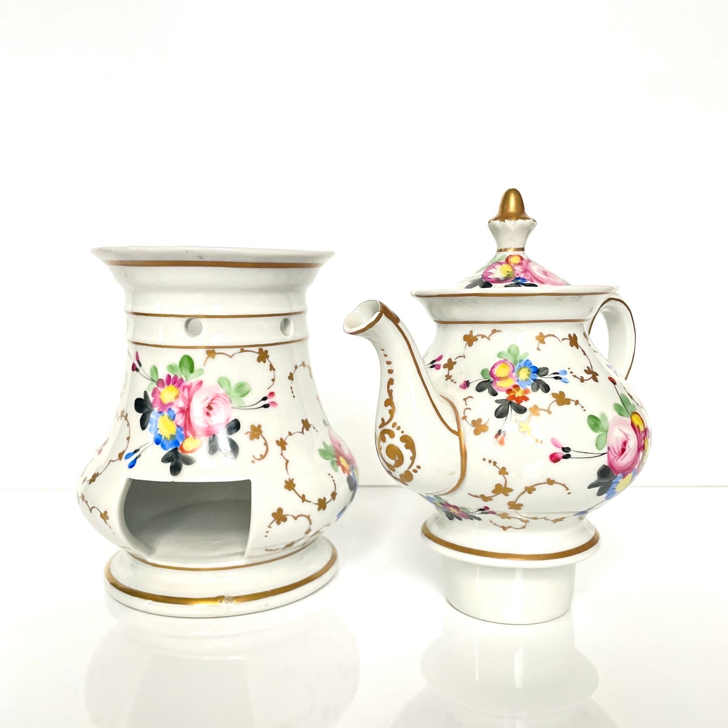 This is a Paris porcelain tisanière (herbal teapot with warmer) from the early 20th century. It features a hand-painted polychrome floral design with gilded accents.