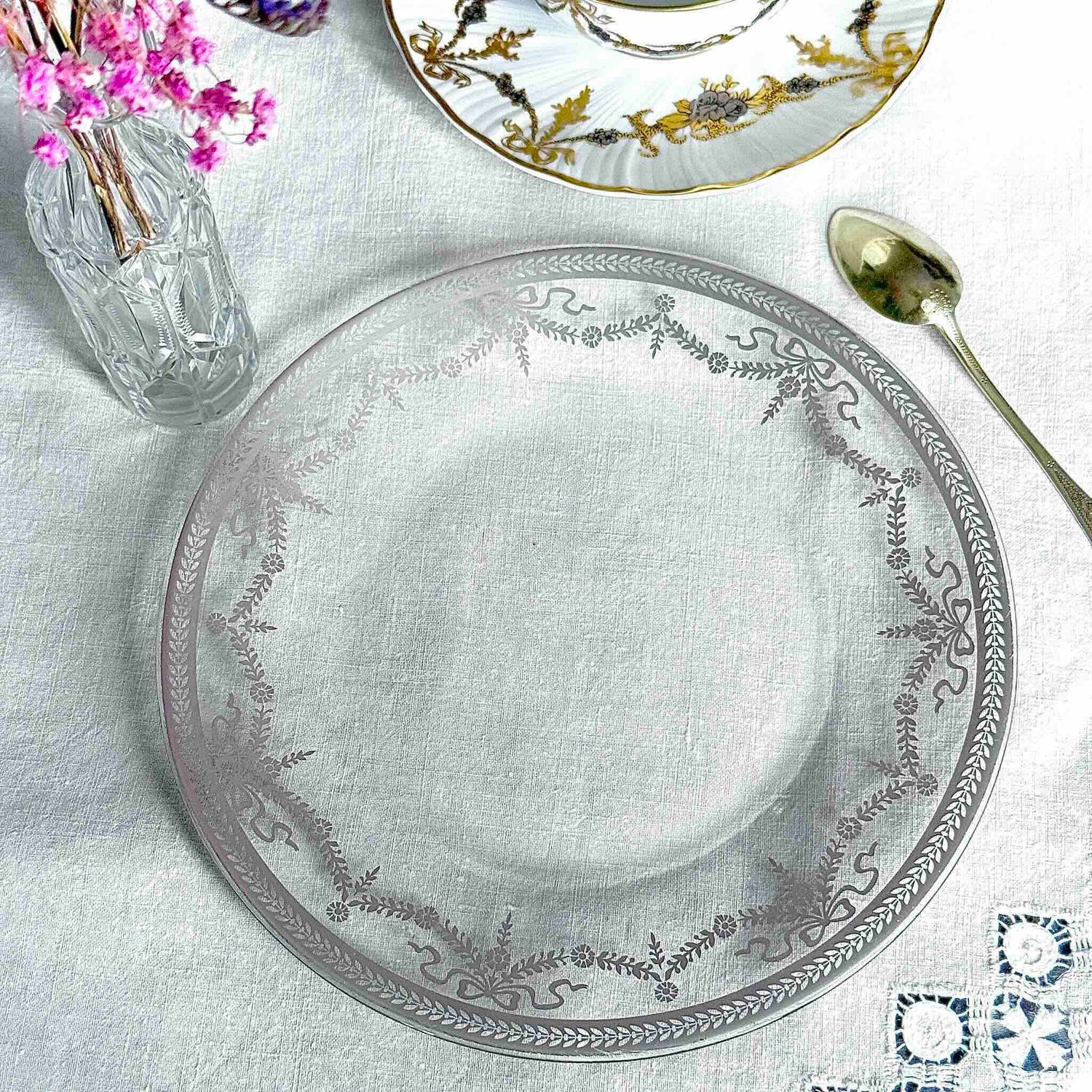 English: Vintage glass dessert plate with silvered ribbon and garland design, elegant and lightly worn. ; Français : Assiette à dessert en verre vintage avec décor argenté de rubans et guirlandes, élégante et en très bon état. ; 日本語： 銀彩のリボンとガーランド模様が施されたヴィンテージのガラス製デザートプレート。上品な印象でコンディション良好。