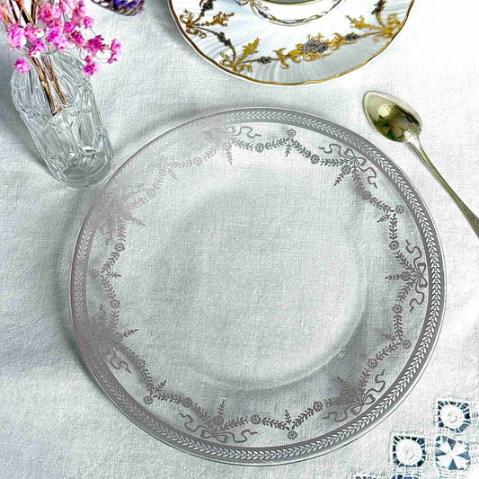 English: Vintage glass dessert plate with silvered ribbon and garland design, elegant and lightly worn. ; Français : Assiette à dessert en verre vintage avec décor argenté de rubans et guirlandes, élégante et en très bon état. ; 日本語： 銀彩のリボンとガーランド模様が施されたヴィンテージのガラス製デザートプレート。上品な印象でコンディション良好。