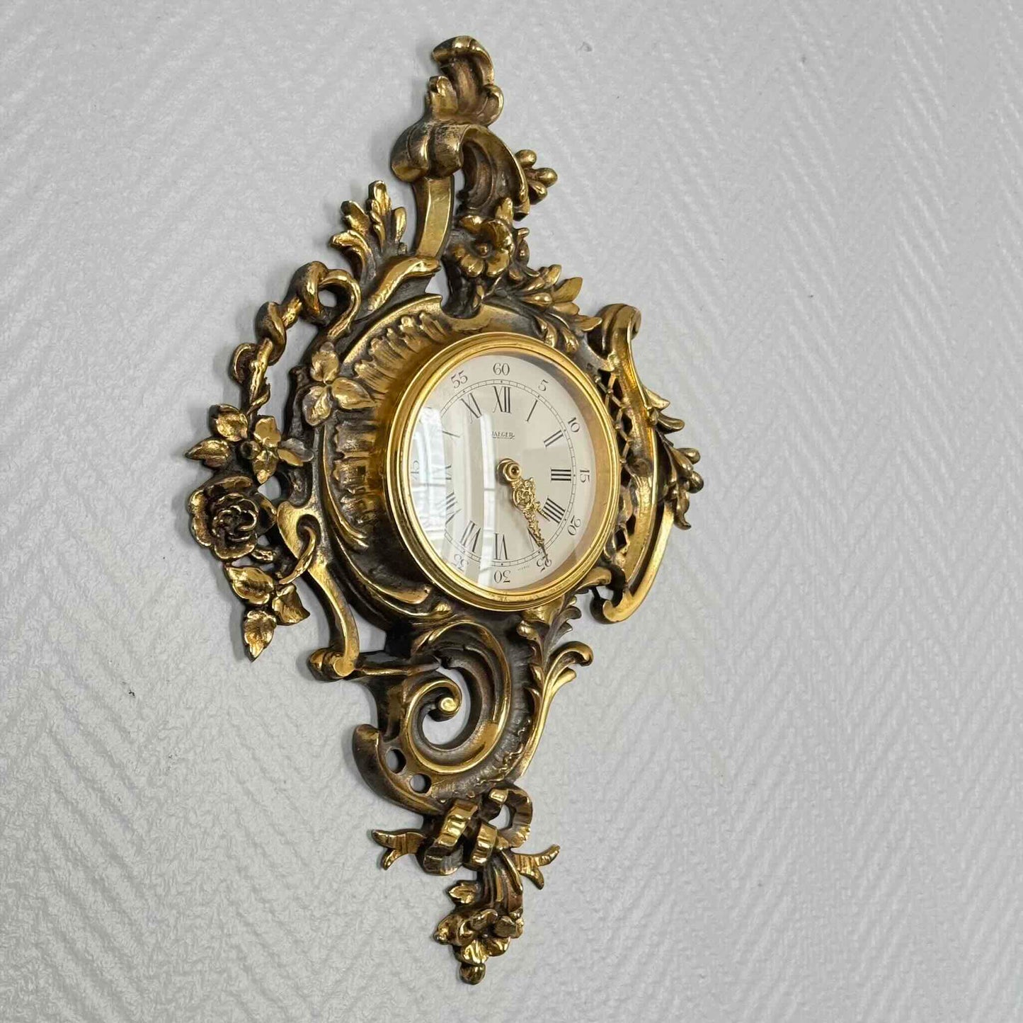 English: Vintage French wall clock by Jaeger in gilded bronze, Rococo style with scrolls, flowers, ribbons, and serpent motif, 1950s–60s. ; 日本語: ジャガー製のフランス製ヴィンテージ壁掛け時計、1950〜60年代、ギルドブロンズ製、ロココ様式のスクロールや花、リボン、蛇の装飾付き。 ; Français : Pendule murale vintage française par Jaeger en bronze doré, style rococo avec volutes, fleurs, rubans et motif de serpent, années 1950–60.