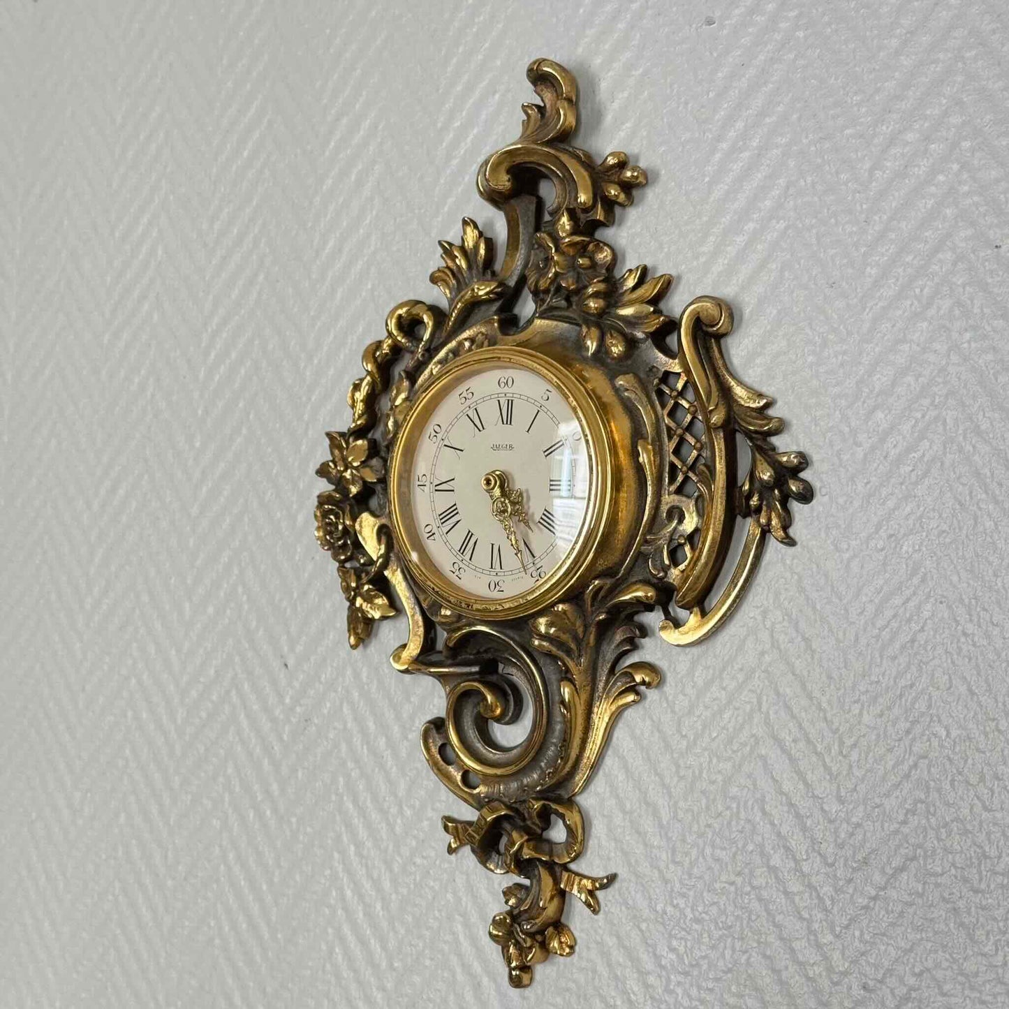English: Vintage French wall clock by Jaeger in gilded bronze, Rococo style with scrolls, flowers, ribbons, and serpent motif, 1950s–60s. ; 日本語: ジャガー製のフランス製ヴィンテージ壁掛け時計、1950〜60年代、ギルドブロンズ製、ロココ様式のスクロールや花、リボン、蛇の装飾付き。 ; Français : Pendule murale vintage française par Jaeger en bronze doré, style rococo avec volutes, fleurs, rubans et motif de serpent, années 1950–60.