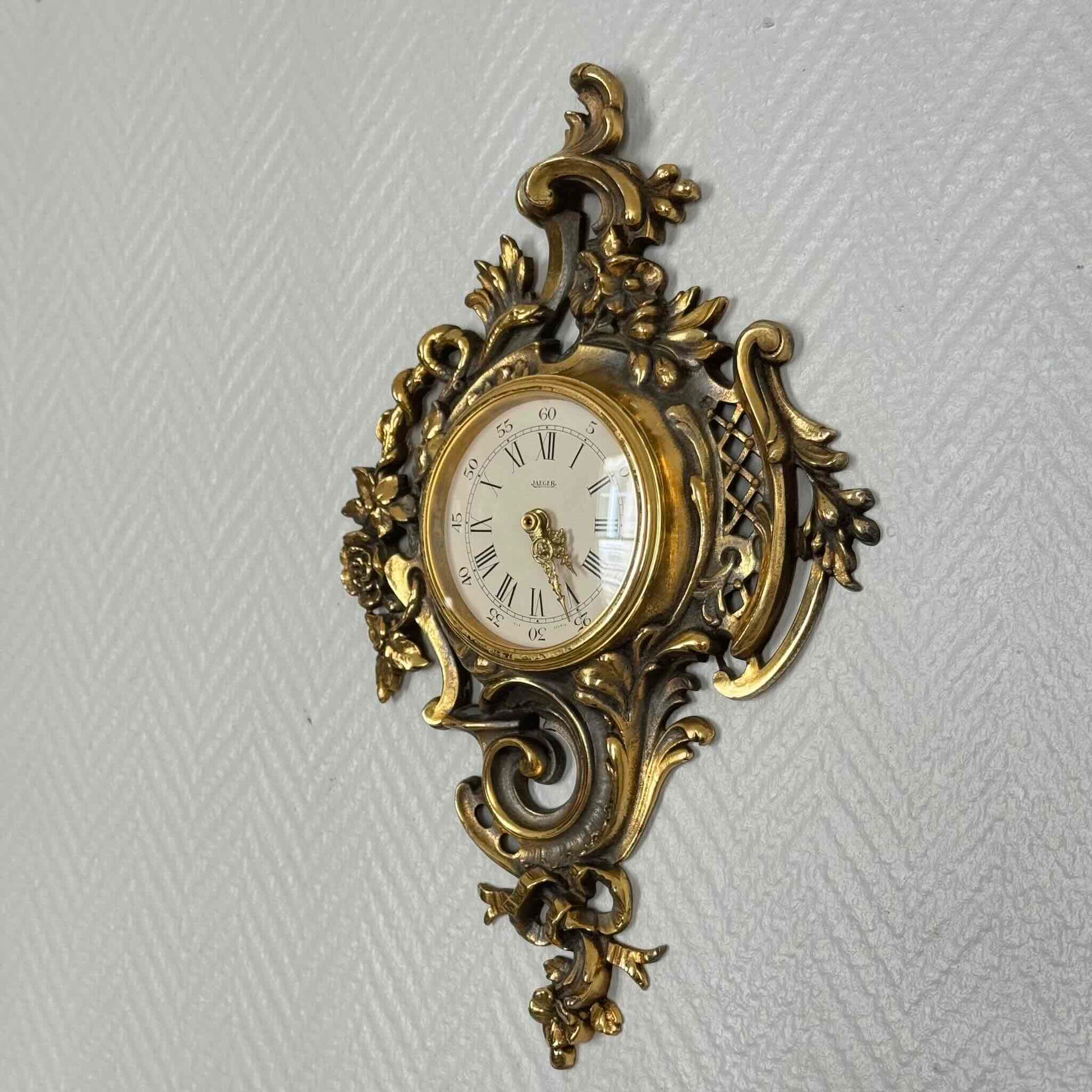 English: Vintage French wall clock by Jaeger in gilded bronze, Rococo style with scrolls, flowers, ribbons, and serpent motif, 1950s–60s. ; 日本語: ジャガー製のフランス製ヴィンテージ壁掛け時計、1950〜60年代、ギルドブロンズ製、ロココ様式のスクロールや花、リボン、蛇の装飾付き。 ; Français : Pendule murale vintage française par Jaeger en bronze doré, style rococo avec volutes, fleurs, rubans et motif de serpent, années 1950–60.