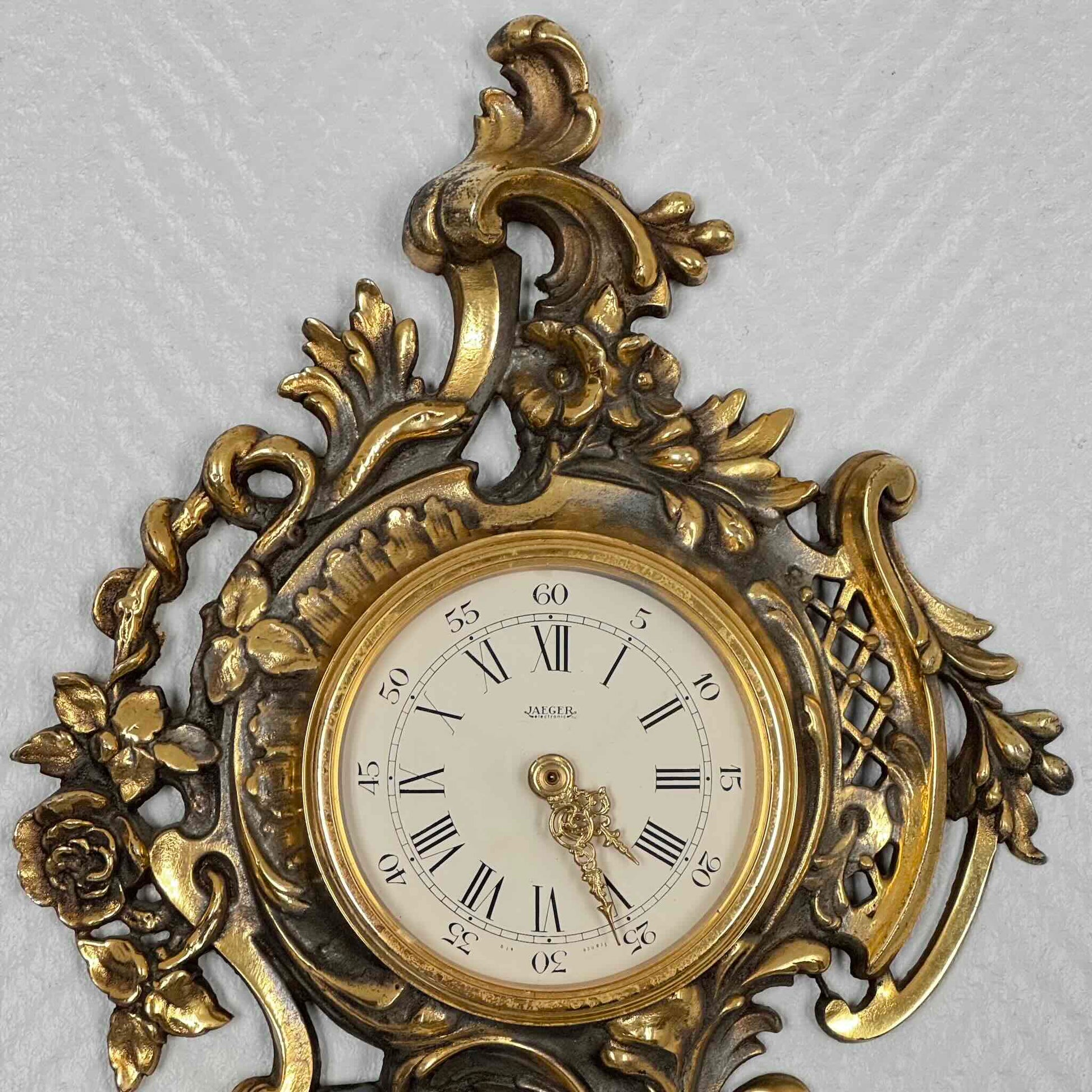 English: Vintage French wall clock by Jaeger in gilded bronze, Rococo style with scrolls, flowers, ribbons, and serpent motif, 1950s–60s. ; 日本語: ジャガー製のフランス製ヴィンテージ壁掛け時計、1950〜60年代、ギルドブロンズ製、ロココ様式のスクロールや花、リボン、蛇の装飾付き。 ; Français : Pendule murale vintage française par Jaeger en bronze doré, style rococo avec volutes, fleurs, rubans et motif de serpent, années 1950–60.