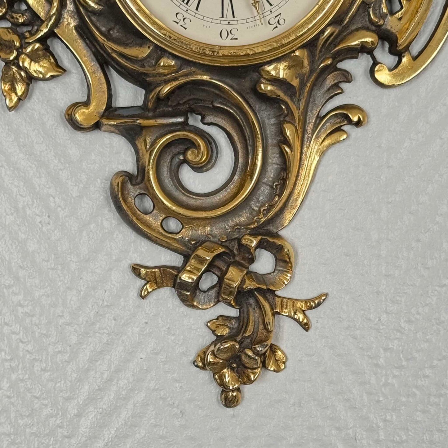 English: Vintage French wall clock by Jaeger in gilded bronze, Rococo style with scrolls, flowers, ribbons, and serpent motif, 1950s–60s. ; 日本語: ジャガー製のフランス製ヴィンテージ壁掛け時計、1950〜60年代、ギルドブロンズ製、ロココ様式のスクロールや花、リボン、蛇の装飾付き。 ; Français : Pendule murale vintage française par Jaeger en bronze doré, style rococo avec volutes, fleurs, rubans et motif de serpent, années 1950–60.