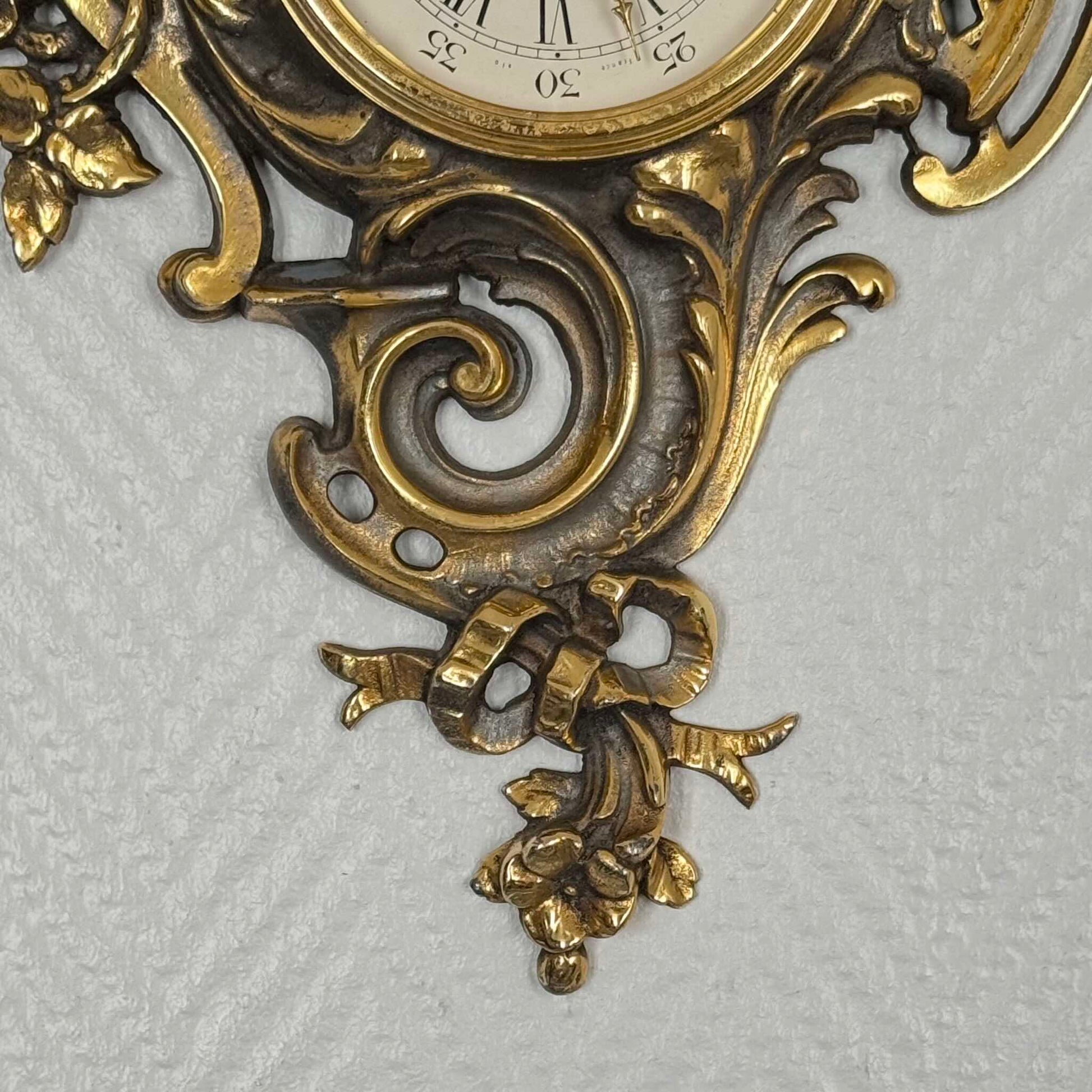 English: Vintage French wall clock by Jaeger in gilded bronze, Rococo style with scrolls, flowers, ribbons, and serpent motif, 1950s–60s. ; 日本語: ジャガー製のフランス製ヴィンテージ壁掛け時計、1950〜60年代、ギルドブロンズ製、ロココ様式のスクロールや花、リボン、蛇の装飾付き。 ; Français : Pendule murale vintage française par Jaeger en bronze doré, style rococo avec volutes, fleurs, rubans et motif de serpent, années 1950–60.