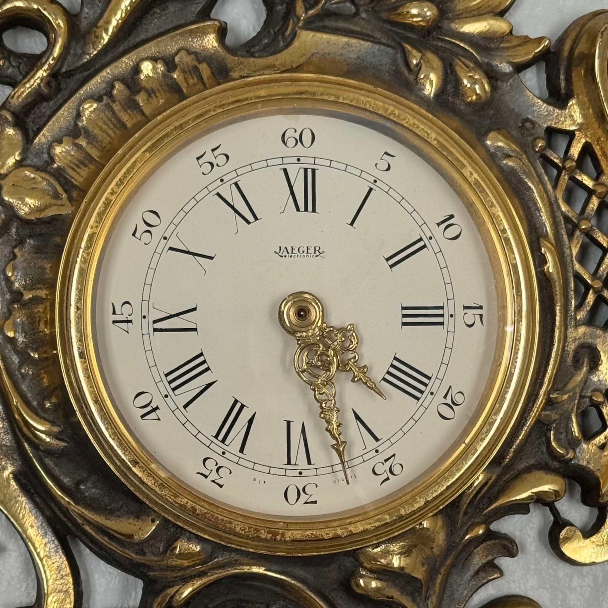 English: Vintage French wall clock by Jaeger in gilded bronze, Rococo style with scrolls, flowers, ribbons, and serpent motif, 1950s–60s. ; 日本語: ジャガー製のフランス製ヴィンテージ壁掛け時計、1950〜60年代、ギルドブロンズ製、ロココ様式のスクロールや花、リボン、蛇の装飾付き。 ; Français : Pendule murale vintage française par Jaeger en bronze doré, style rococo avec volutes, fleurs, rubans et motif de serpent, années 1950–60.